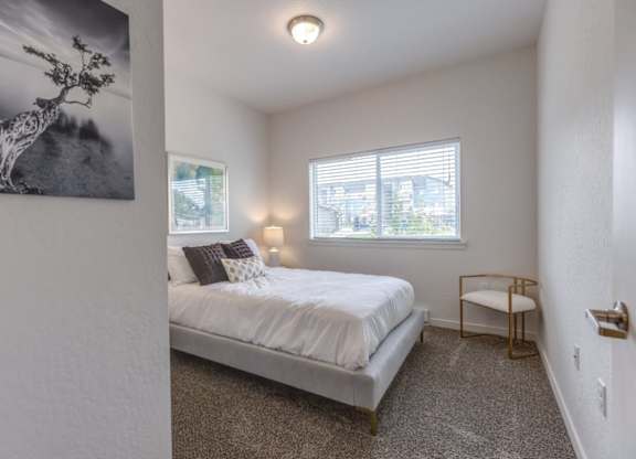 A bedroom with a bed, a chair, and a window with blinds.