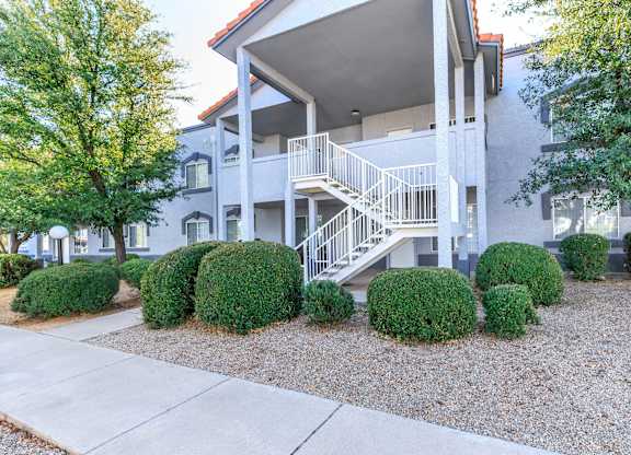 A modern house with a white staircase and green bushes in front.
