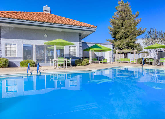 A swimming pool in front of a house with a red roof.
