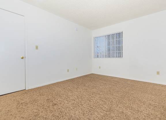 A room with a carpeted floor and a window with bars.