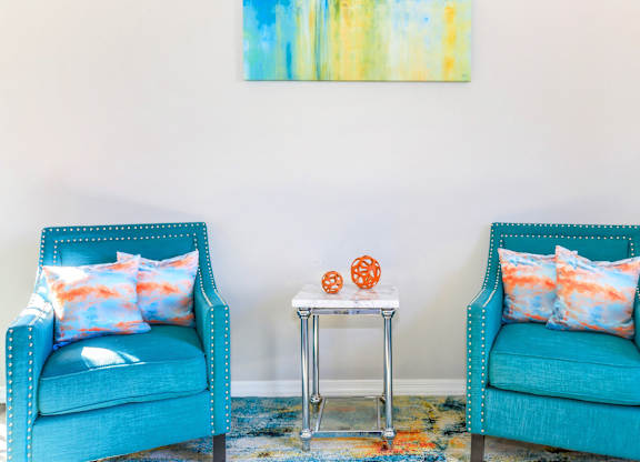 Two blue chairs with pillows and a small table between them.