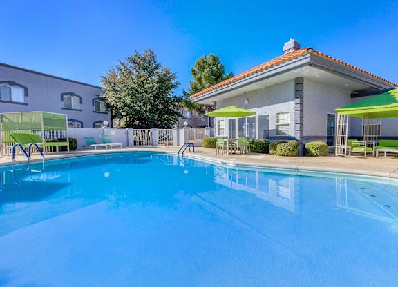 A swimming pool in front of a house with a green umbrella.