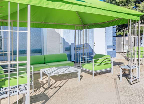A patio with a green umbrella and matching chairs.