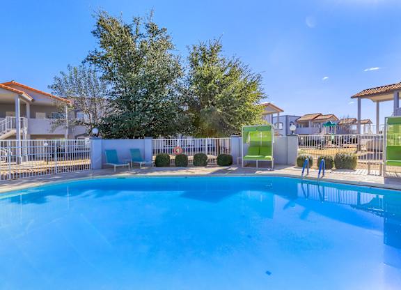 A large swimming pool surrounded by a white fence and green chairs.