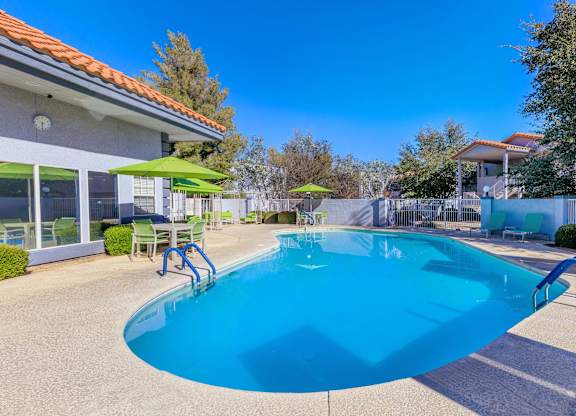 A swimming pool with a blue tinted water and a green umbrella.