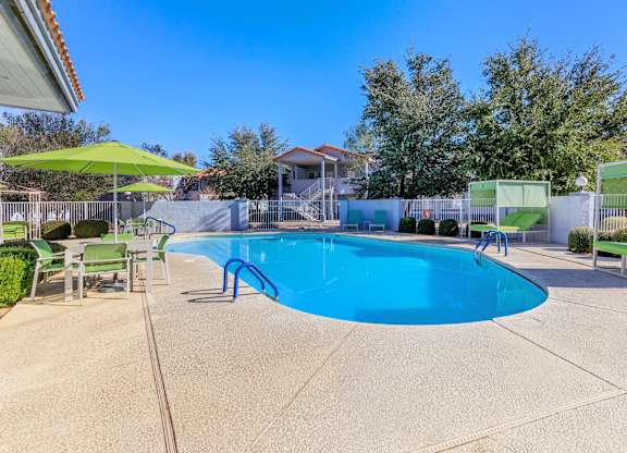 A blue swimming pool surrounded by a green fence and trees.