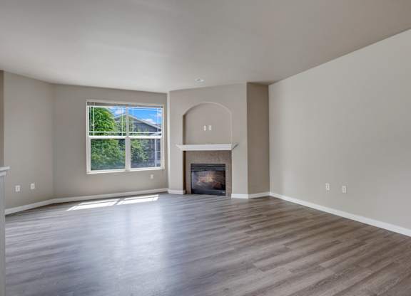 A large empty room with a fireplace and a window.