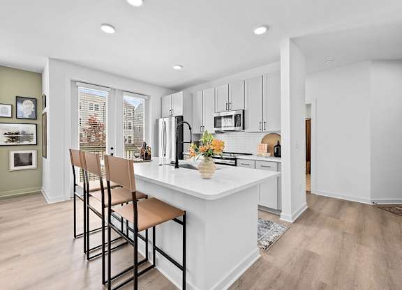 A kitchen with a white island and brown barstools.