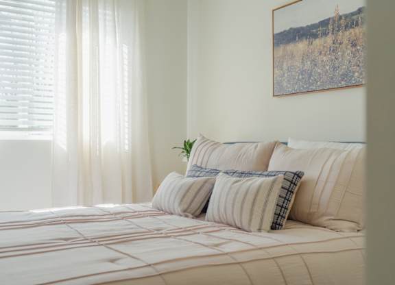 A bed with a white comforter and striped pillows with a plant on it.