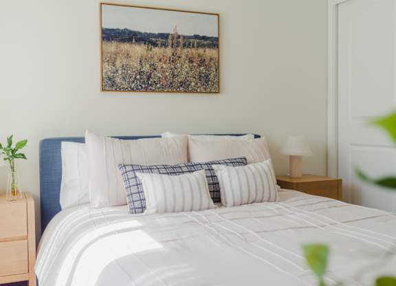A bed with a white comforter and a landscape picture on the wall.