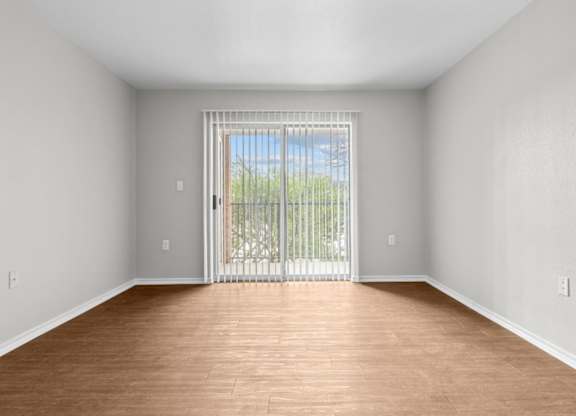 A room with wooden floors and a sliding glass door leading to a balcony.