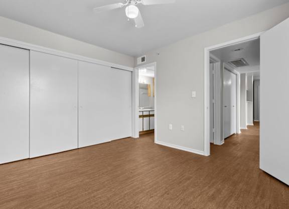 A room with white walls and wooden flooring with a ceiling fan.