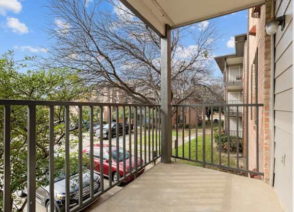 A balcony with a black railing and a view of a parking lot and trees.