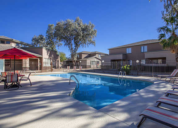A pool surrounded by lounge chairs and a red umbrella.