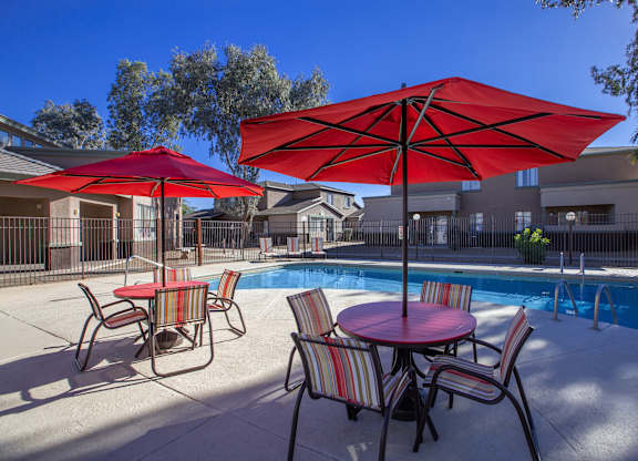 A red umbrella is in the foreground of a pool area.