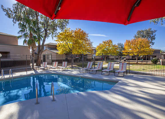 A pool with a red canopy and lounge chairs.