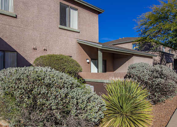 A house with a brown exterior and a green bush in front.