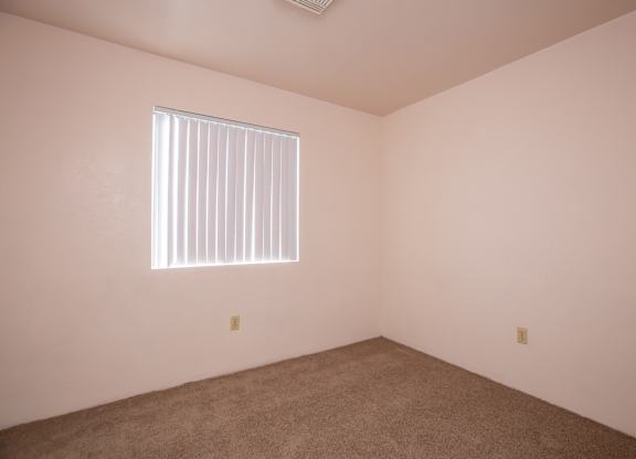 A room with a carpeted floor and a window with blinds.