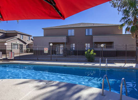 A swimming pool is surrounded by a fence and a building.