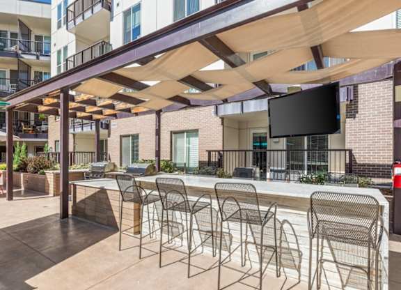 A patio with a bar and chairs under a wooden canopy.