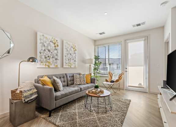 A living room with a grey couch, a round table, and a flat screen TV.