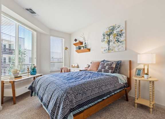 A bedroom with a bed, nightstand, and a painting on the wall.