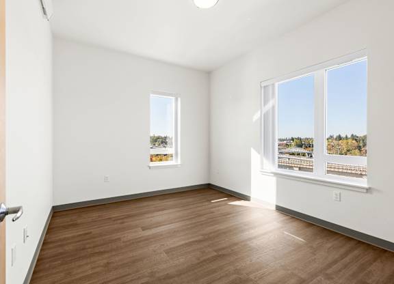 A room with a wooden floor and a window showing a view of trees.