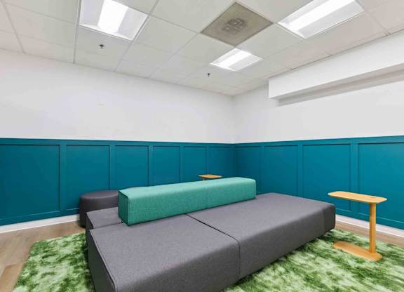 A bedroom with a bed, a green rug, and a small table.