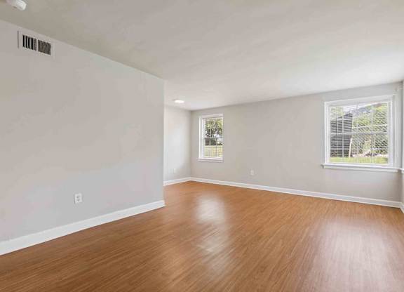 A room with wooden flooring and two windows.