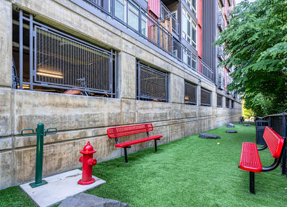A red fire hydrant sits next to a red bench in a small grassy area.