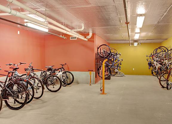 A room with orange walls and a white floor has bicycles parked against the walls.