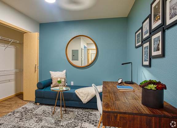 A blue couch with a white pillow and a round mirror on the wall.