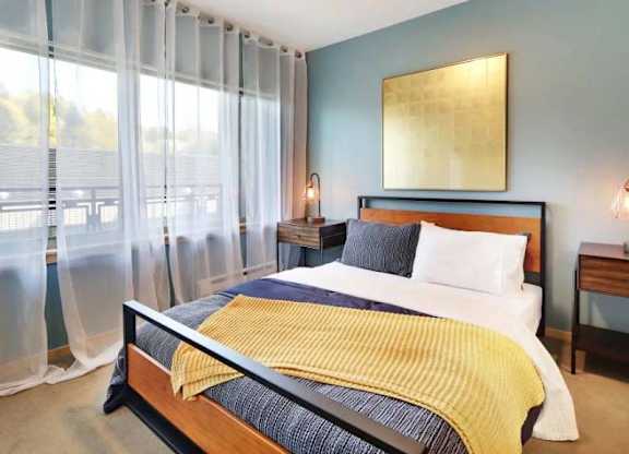A bedroom with a bed, nightstands, and a large window with sheer curtains.