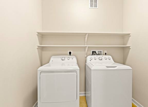 In-unit white washer and dryer set with shelving above and white walls at Sylvan Uptown,Colorado, Denver