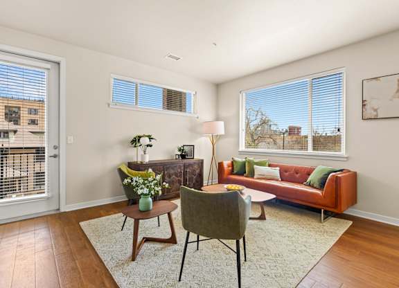 Spacious living room with a couch and chairs surrounding in natural light from the windows and door leading out to the balcony at Sylvan Uptown, Colorado
