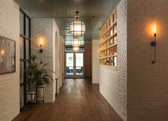 Long white brick hallway with wood flooring and geometric pendant lighting leading to resident lounge at Sylvan Uptown, Colorado
