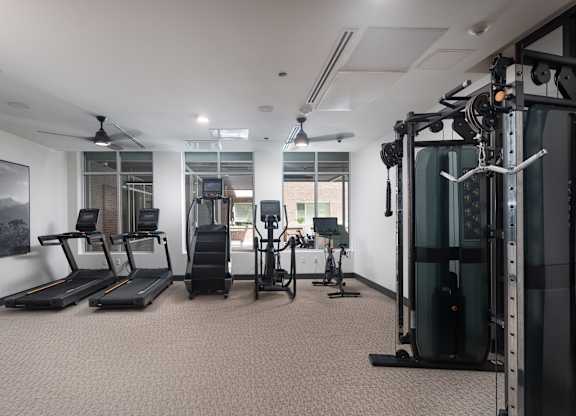 Resident gym with two treadmills, a stairstepper, an elipitcal, and a stationary bike with a television facing the large windows weights and mirrors in a room with a window at Sylvan Uptown, Denver