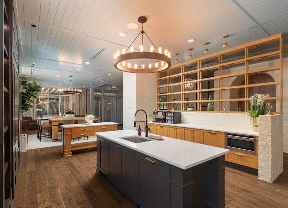 Gorgeous resident kitchen and lounge area with a patterned wood and brick half-wall, dark island cabinetry with gold hardware and sink, and view into the chic seating area at Sylvan Uptown, Denver, CO