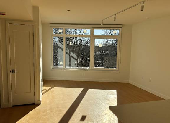 A room with a door and a window with a view of trees outside. at 605 Concord at Fresh Pond Apartments, Cambridge, Massachusett