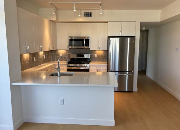 A kitchen with a stainless steel refrigerator and a microwave above the stove at 605 Concord at Fresh Pond Apartments, Cambridge, MA, 02138