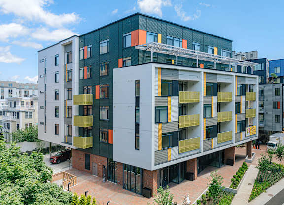 A modern multi-story building with balconies and a mix of grey, yellow, and orange colors at 605 Concord at Fresh Pond, Massachusetts, 02138