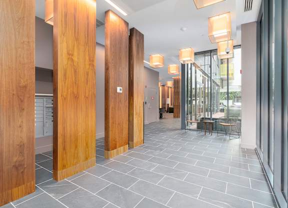 A modern lobby with wooden columns and grey tiled flooring  at 605 Concord at Fresh Pond Apartments, Massachusetts