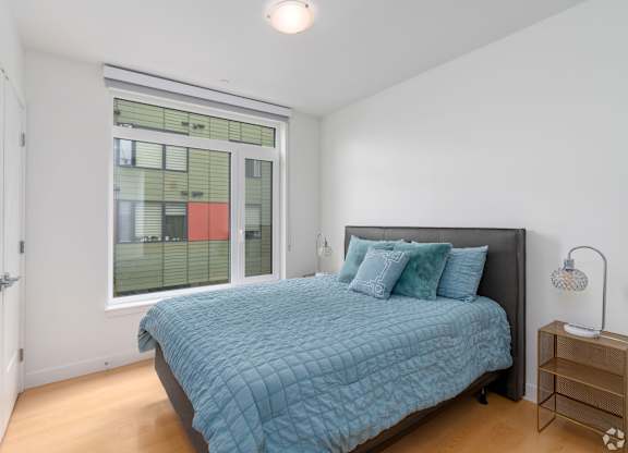 A bedroom with a bed, nightstand, and window  at 605 Concord at Fresh Pond Apartments, Massachusetts