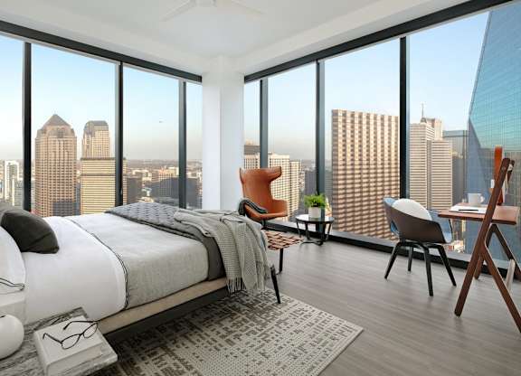 A bedroom with a large bed and a city view through the windows.