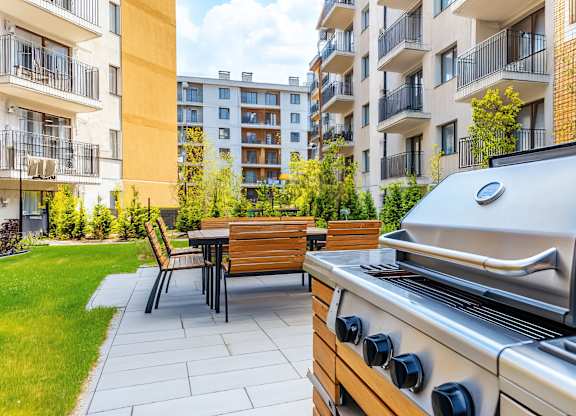 A grill is in the foreground of a patio with a table and chairs.