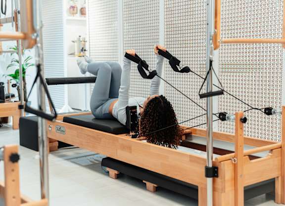 A person is doing Pilates on a reformer in a well-lit room.