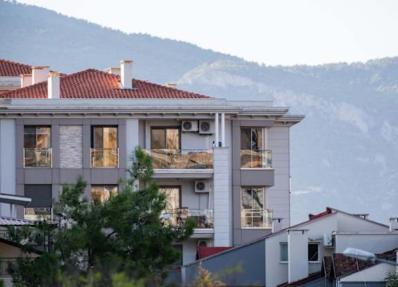 A white building with red roof tiles sits in front of a mountain.