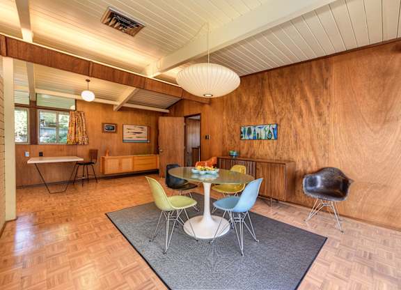 A room with a wooden wall and a white table with four chairs.