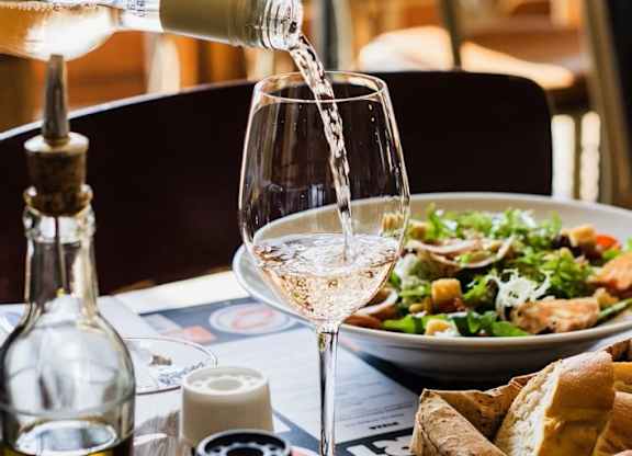 White wine being poured into a glass with a salad and bread on the table.