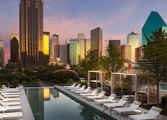 A pool with lounge chairs and a city skyline in the background.
